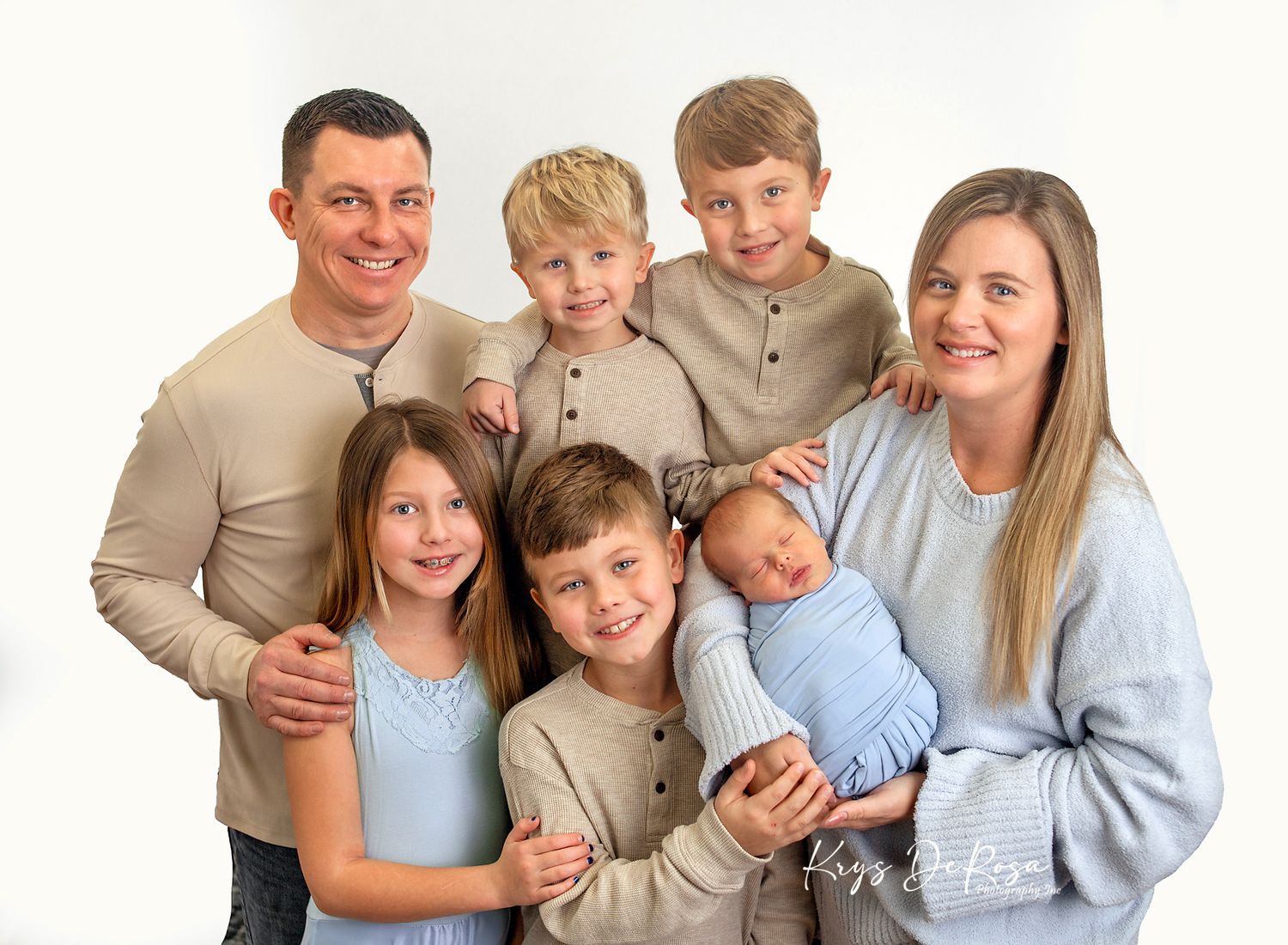 Happy family of seven posing together, parents with four children and a newborn baby, in a bright white studio setting.