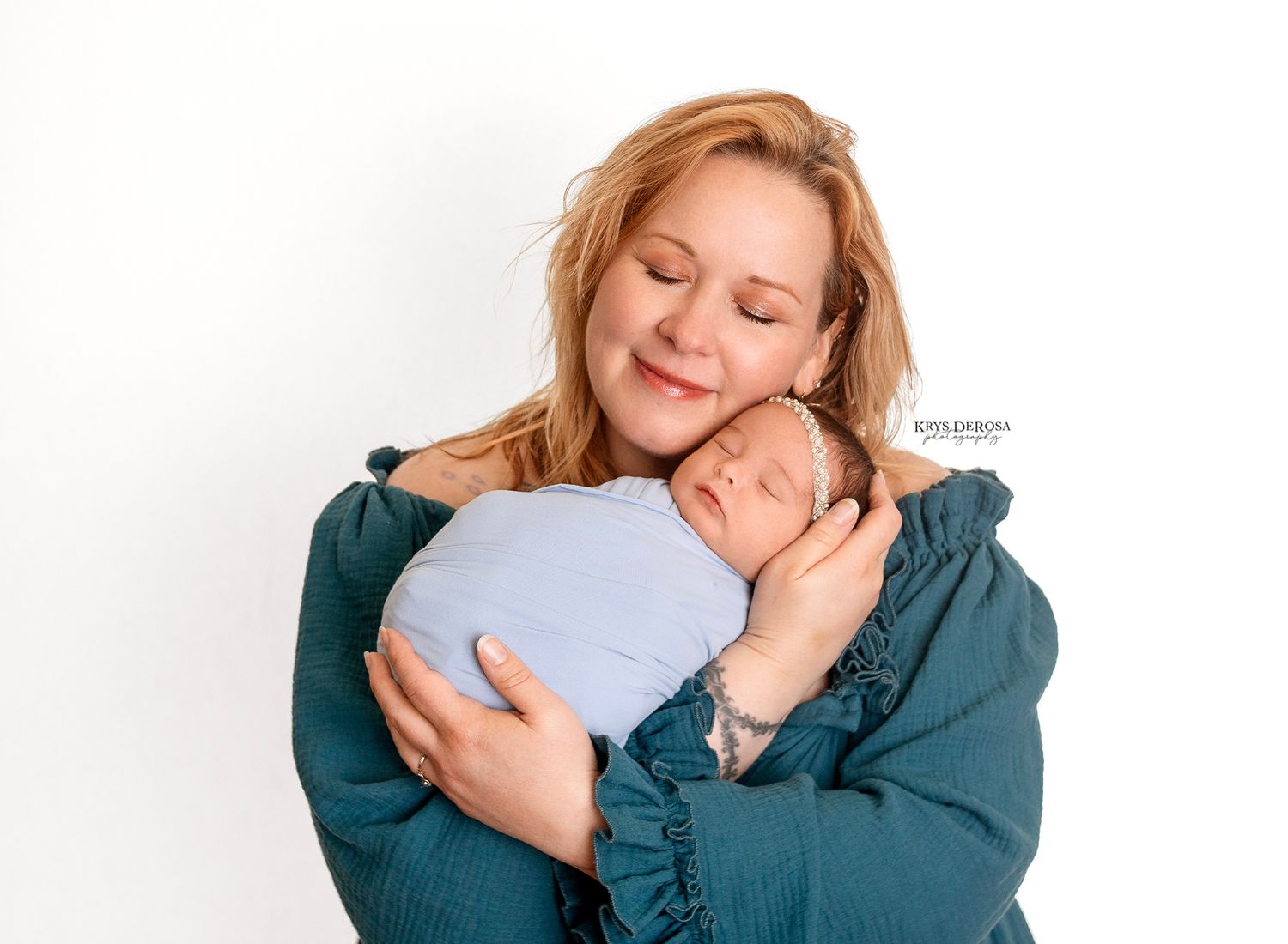 Mother with eyes closed smiling while cradling sleeping newborn baby wrapped in light blue swaddle.