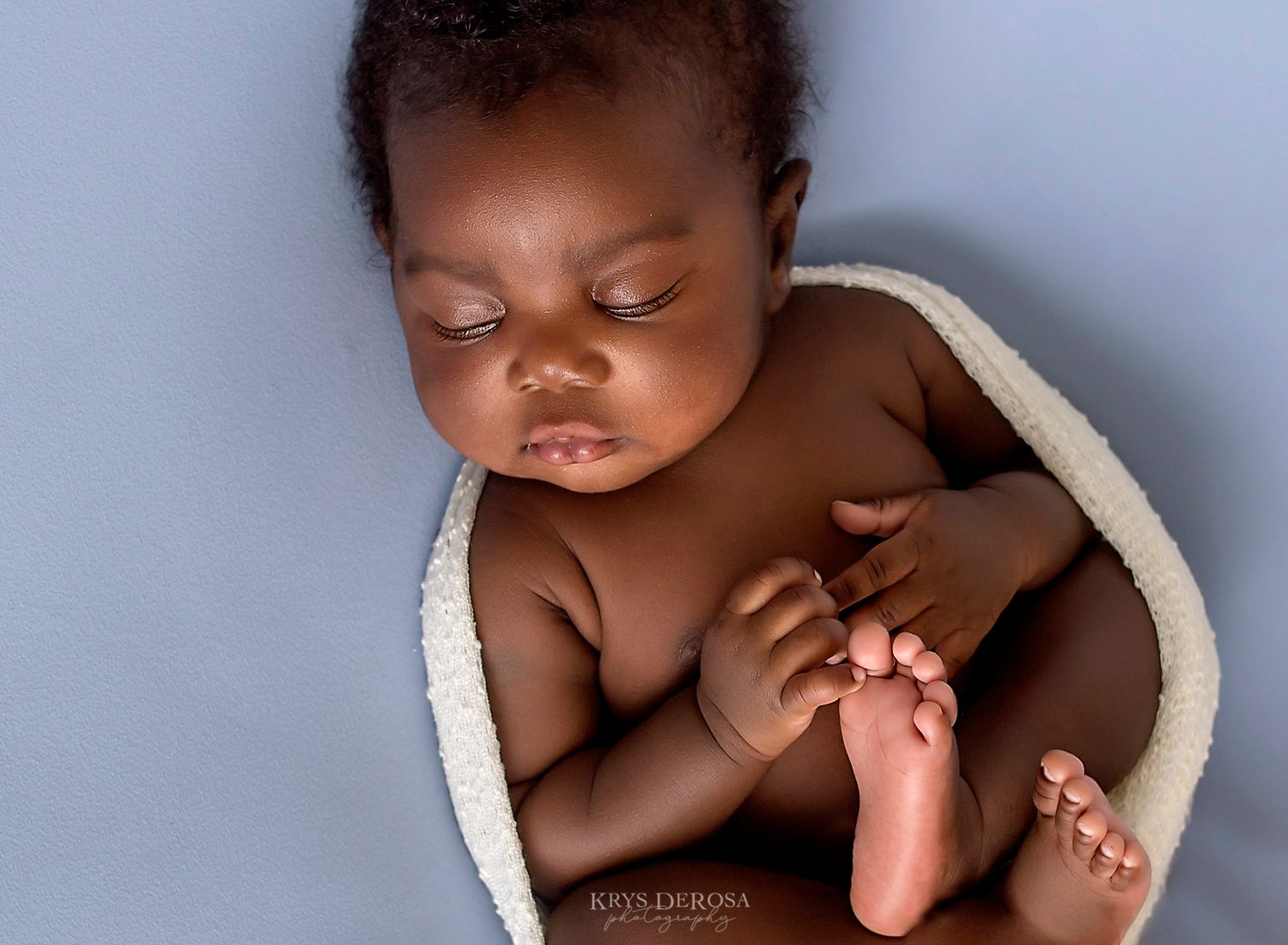 Newborn baby sleeping wrapped in a cozy white blanket on a soft blue background.