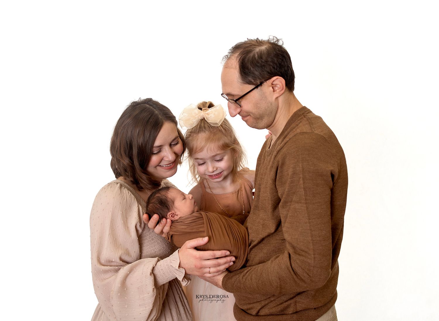 Family of four posing for a professional portrait, parents holding newborn and toddler girl, against white background.