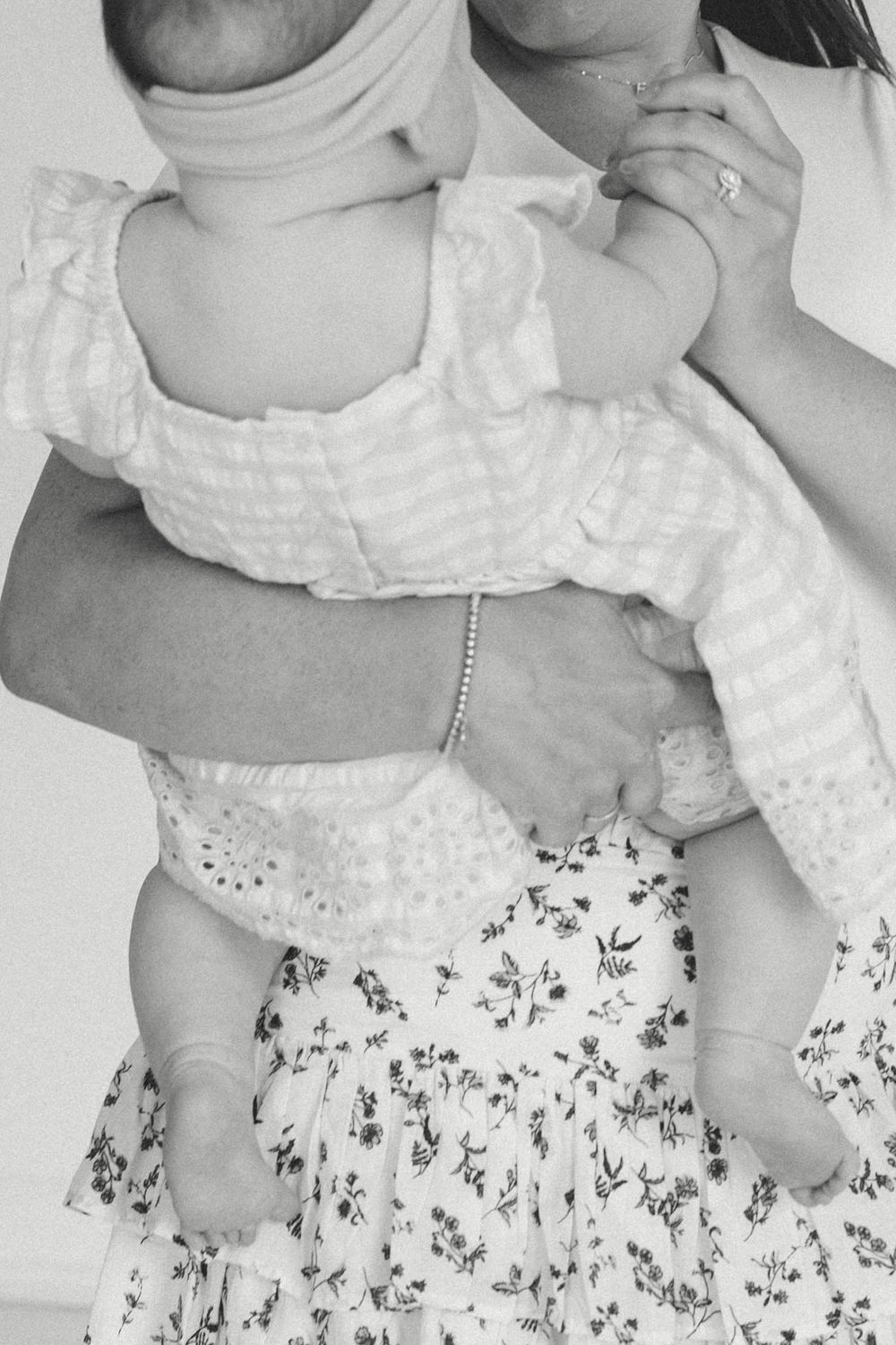 Black and white photo of a mother holding her newborn baby dressed in a white floral outfit.