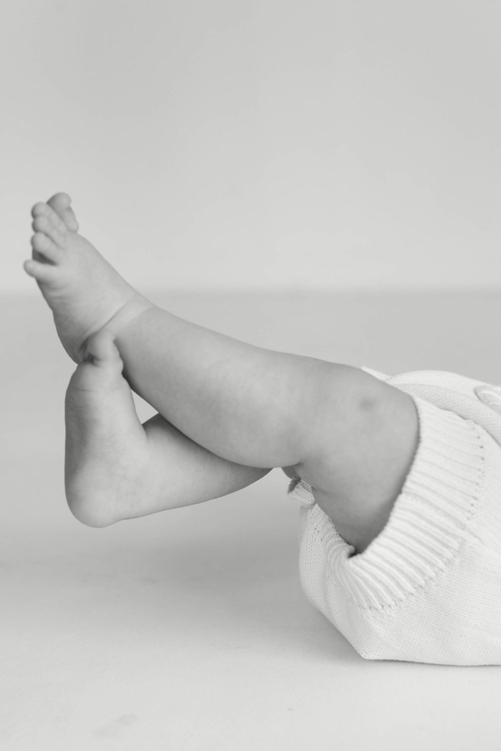 Black and white close-up of a baby lying down with legs raised in a knit outfit.