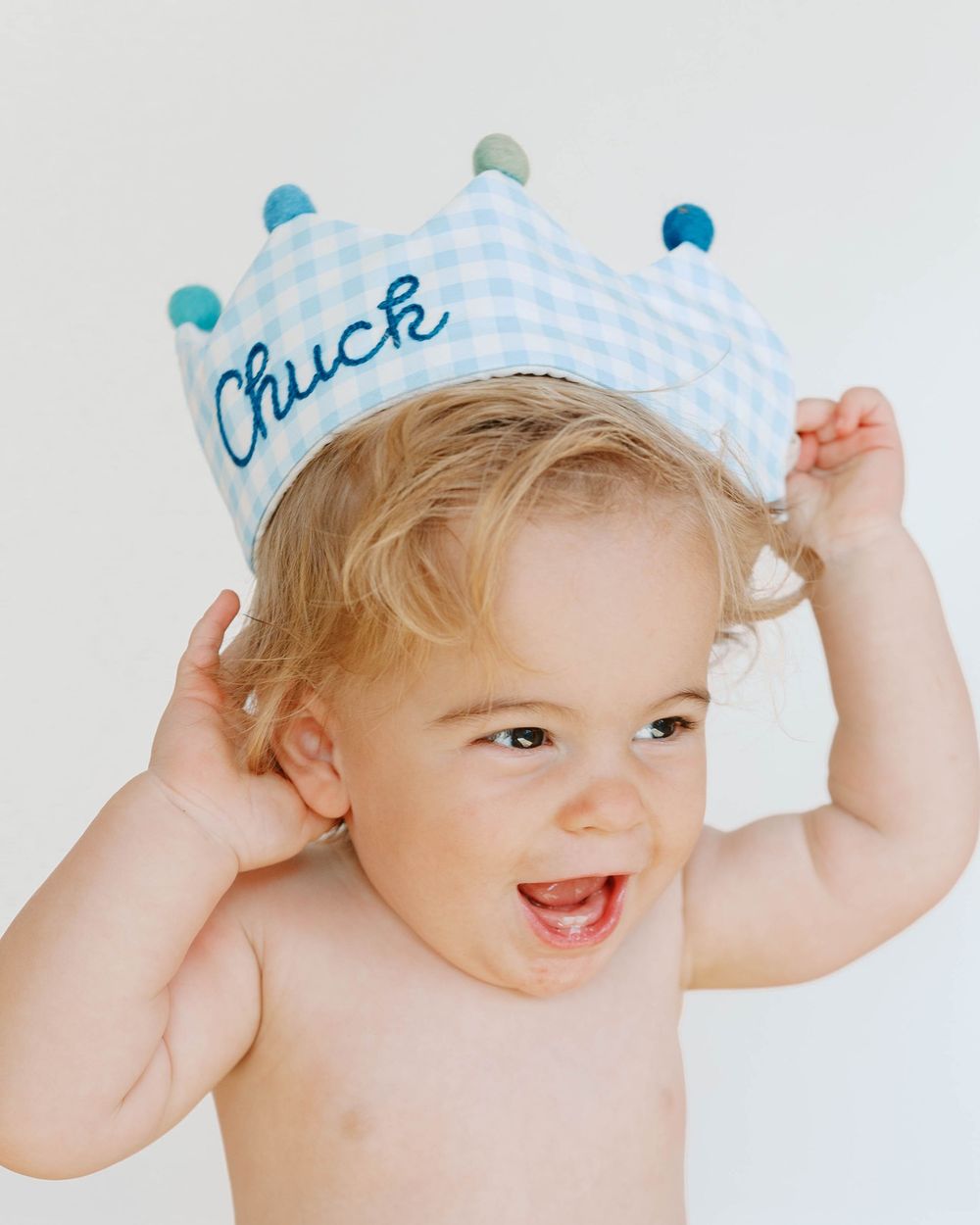 Smiling toddler wearing a blue gingham crown hat embroidered with the name Chuck.