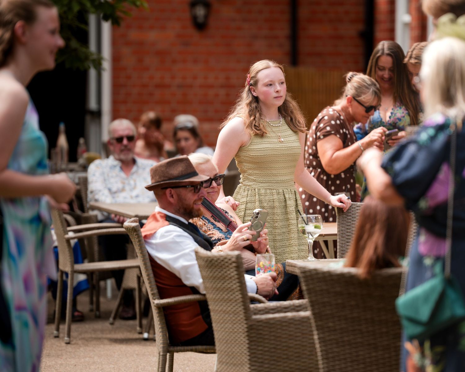 Guests socializing at an outdoor summer garden party, seated at wicker chairs on a sunny patio.
