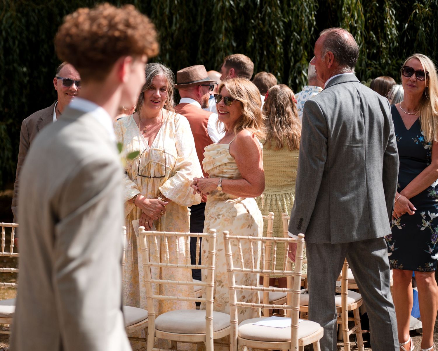 Guests socializing at an outdoor wedding ceremony, seated on elegant chiavari chairs in a sunny garden setting.