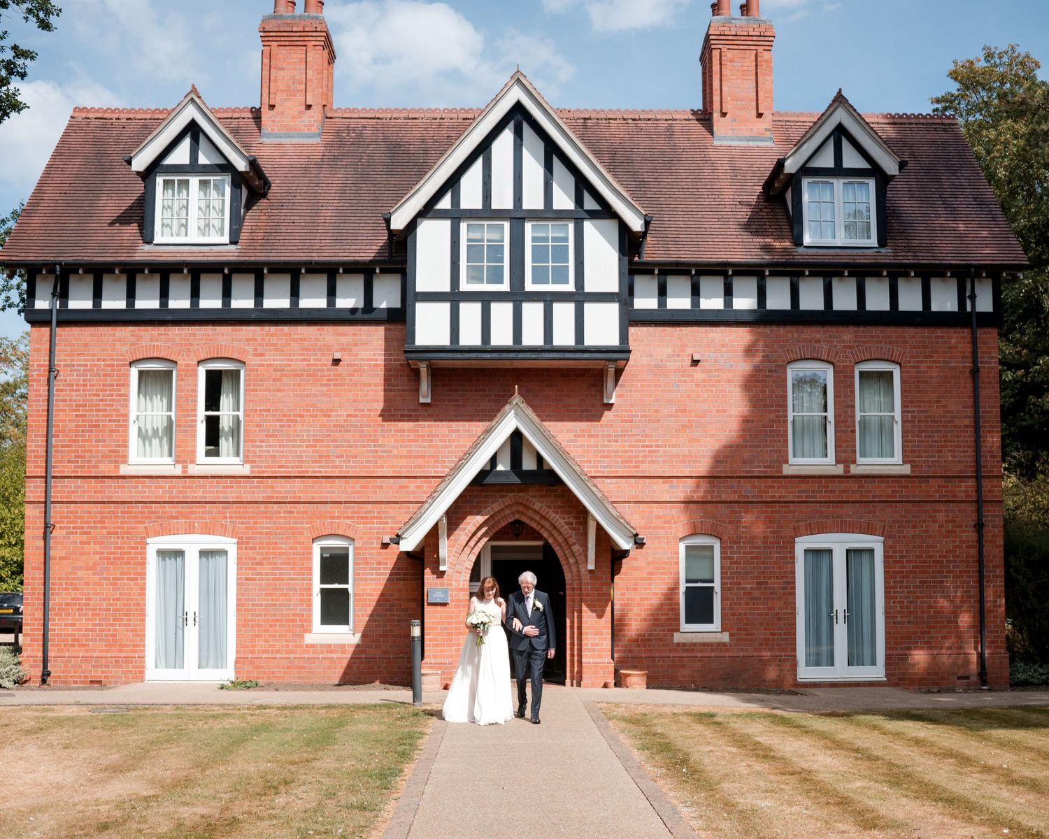 Bride and groom standing outside a stunning Tudor-style red brick wedding venue on a sunny day.
