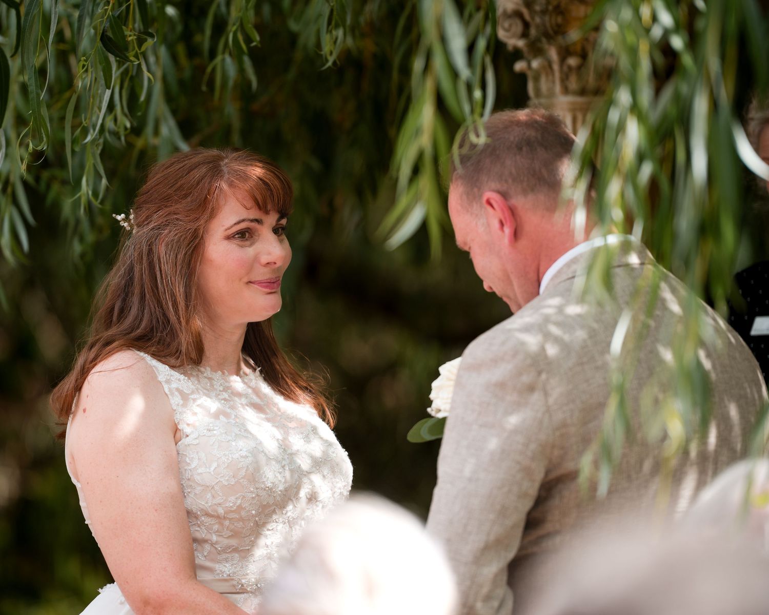 Bride and groom exchange vows outdoors under weeping willow tree during romantic wedding ceremony.