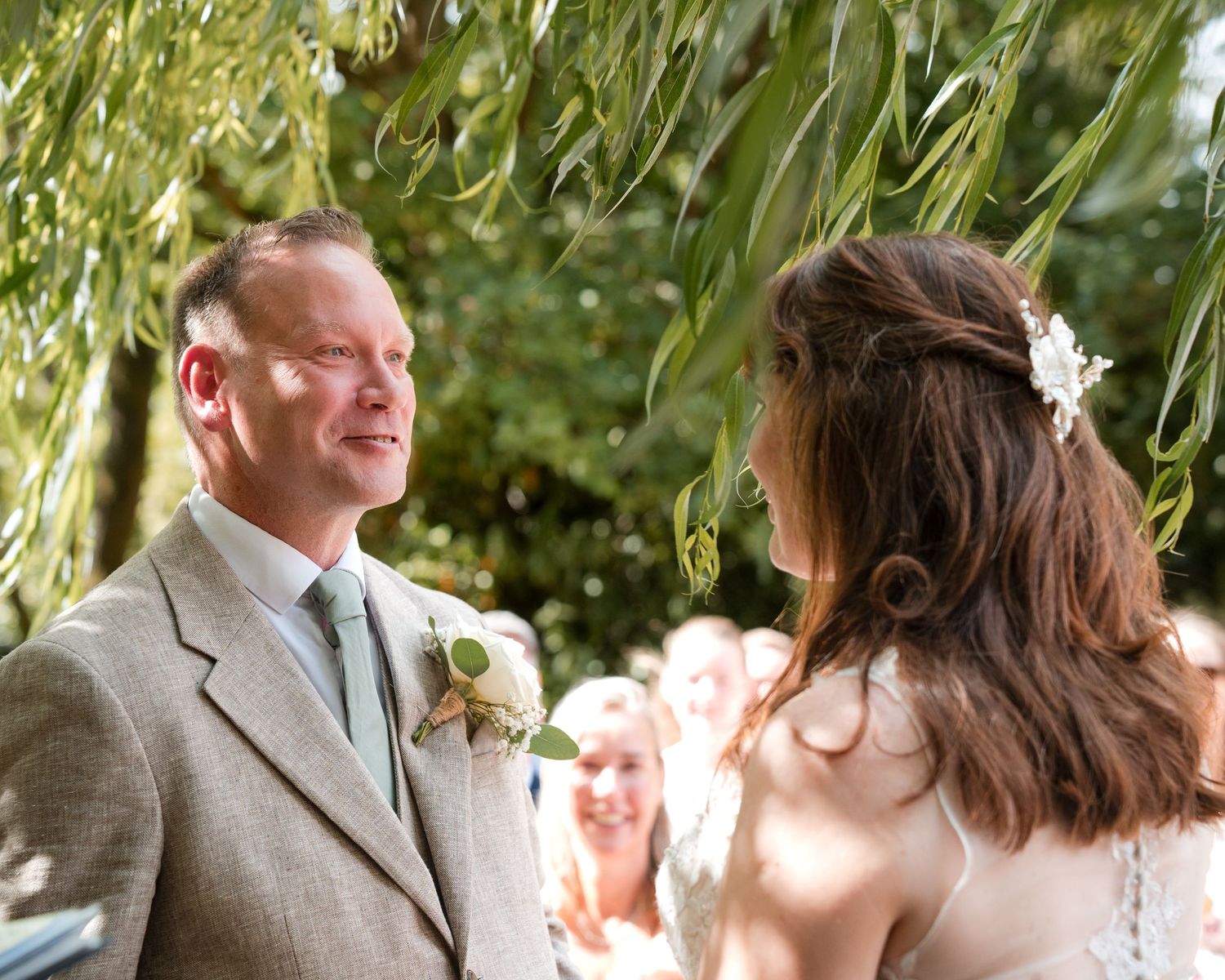 Bride and groom exchange vows outdoors under willow tree at elegant garden wedding ceremony.