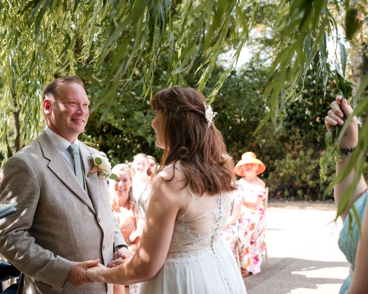 Bride and groom holding hands during outdoor wedding ceremony with guests in background.