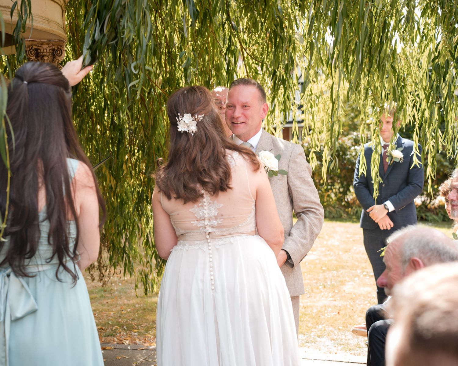 Bride and groom share a romantic moment during outdoor wedding ceremony under a weeping willow tree.