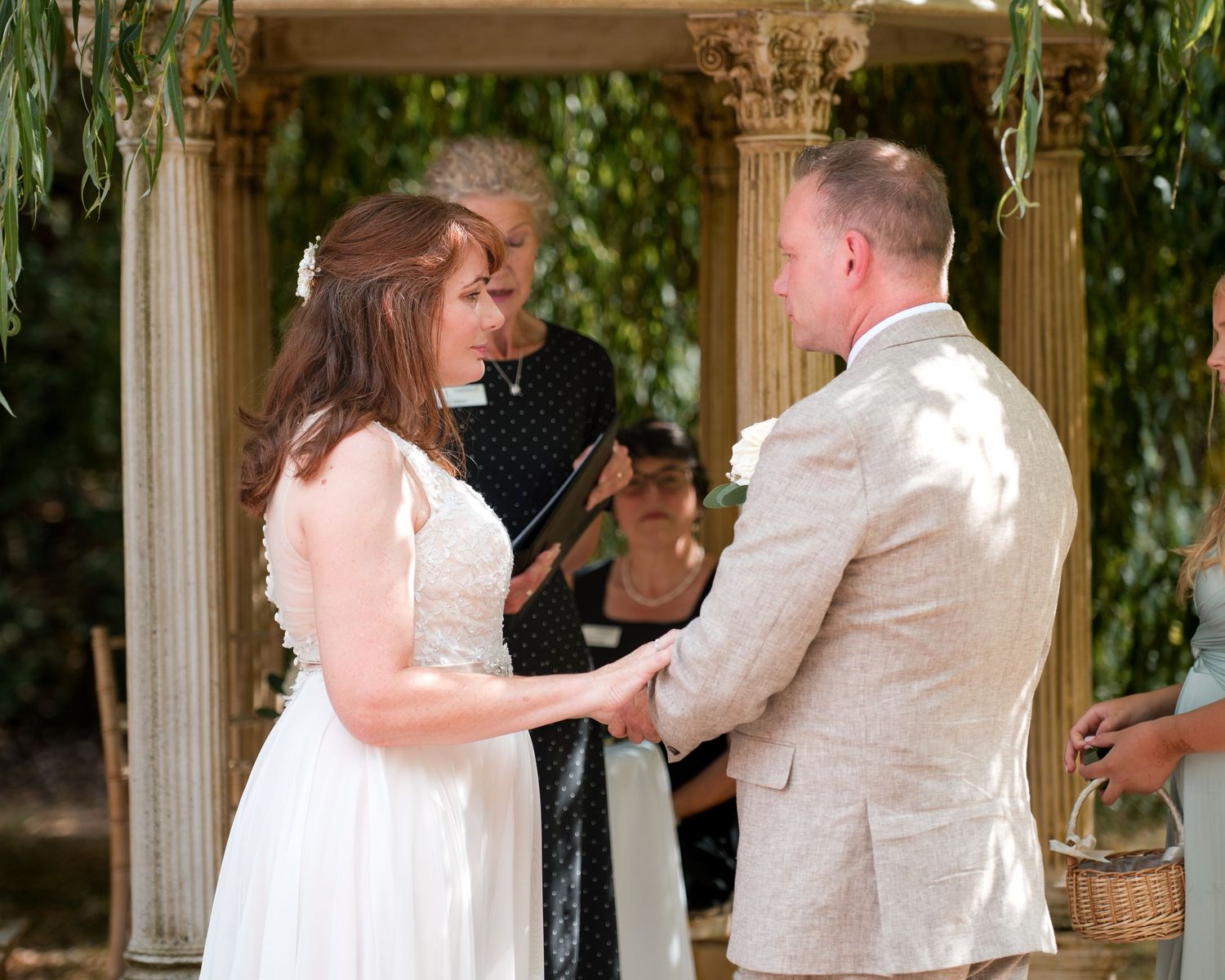 Bride and groom exchange vows outdoors at a garden wedding ceremony with an officiant and floral arbor backdrop.