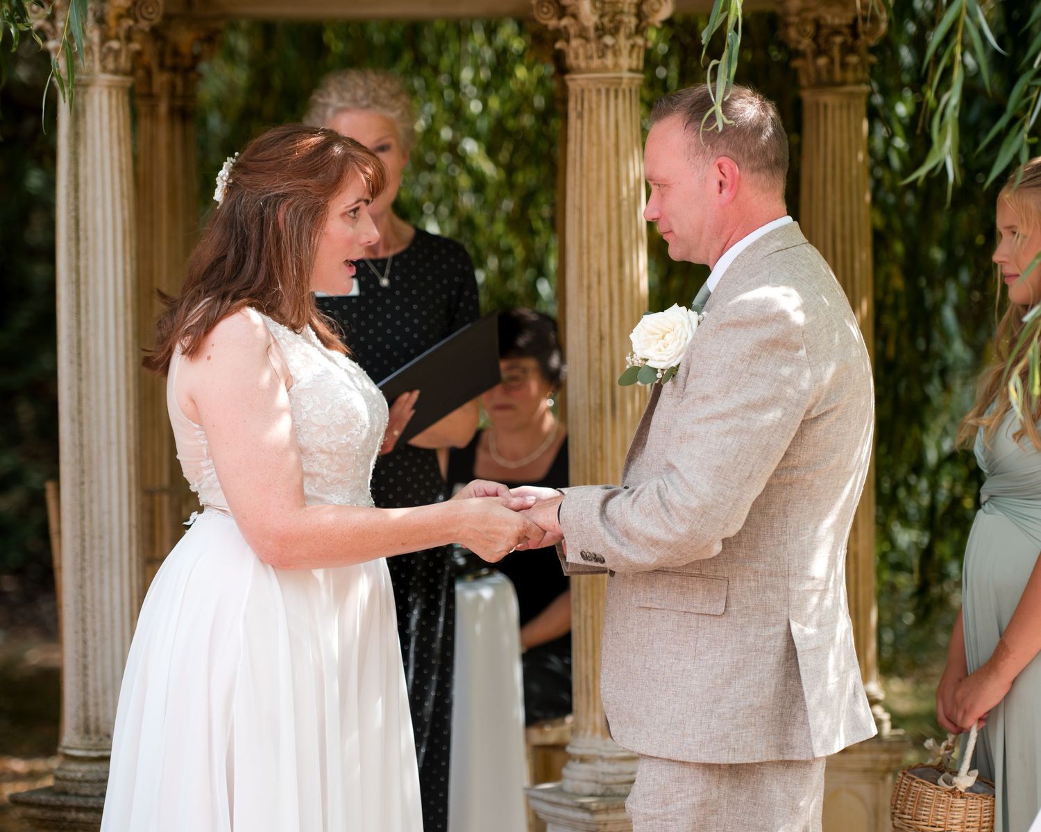 Bride and groom exchange vows outdoors at elegant garden wedding ceremony with officiant and guests.