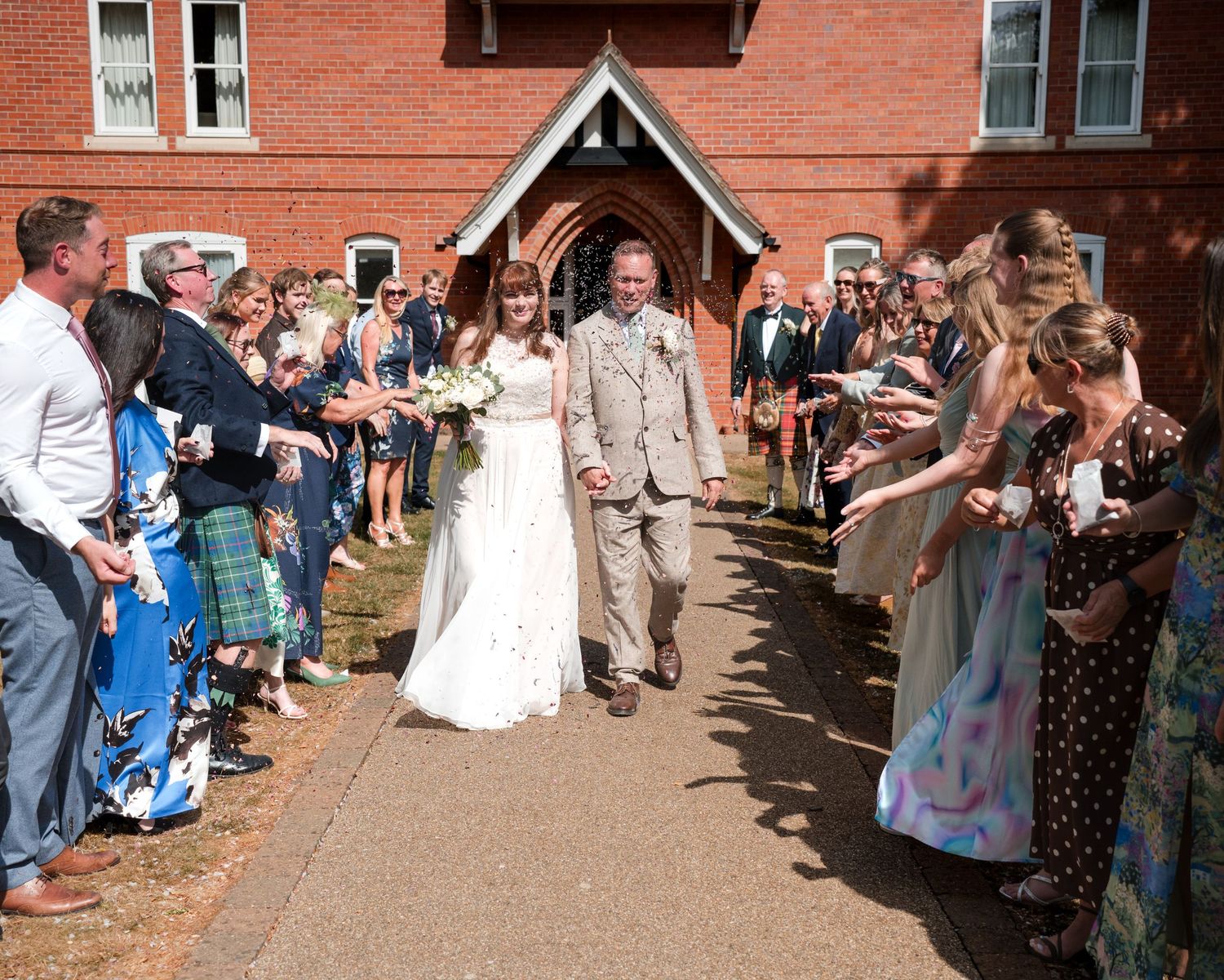 Newlywed couple exits church through cheering guests after wedding ceremony on sunny day.