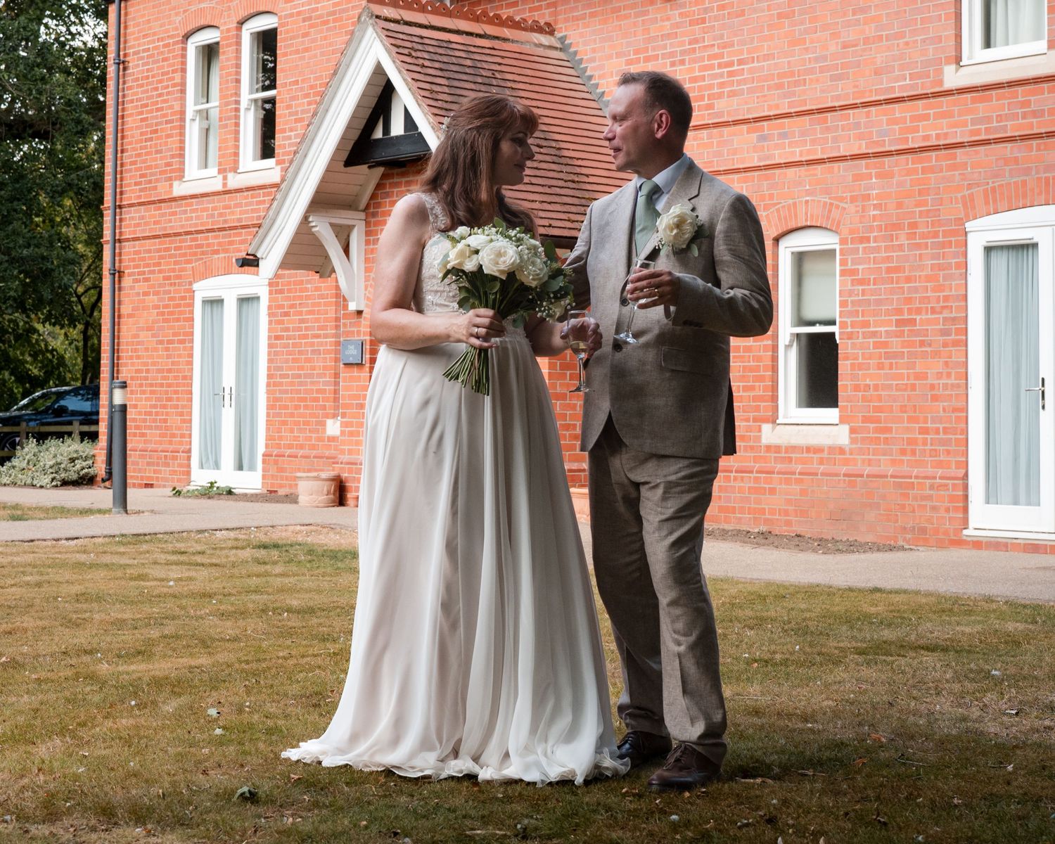 Bride and groom standing together outside a red brick building on their wedding day.