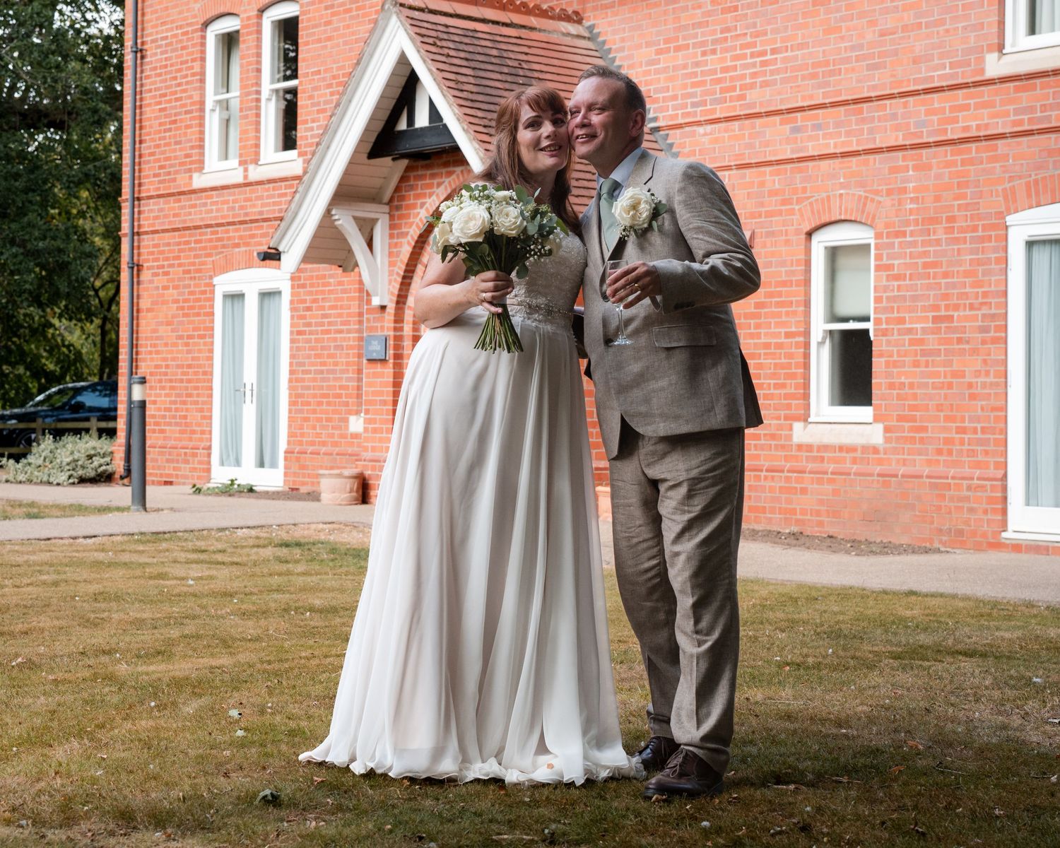 Bride and groom posing together outside a red brick building on their wedding day.
