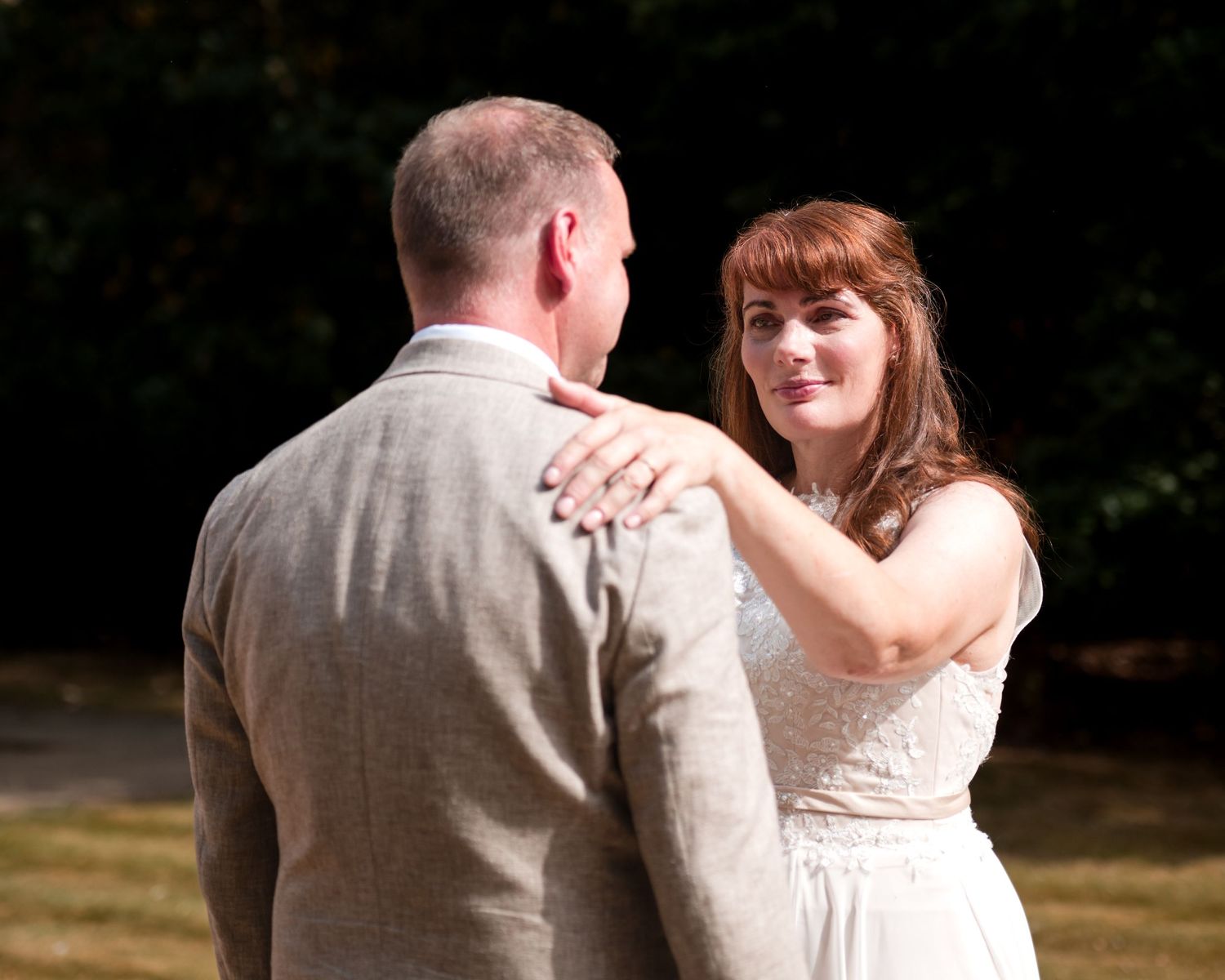 Bride and groom share a tender moment outdoors, with the bride smiling warmly in a white dress during their wedding.