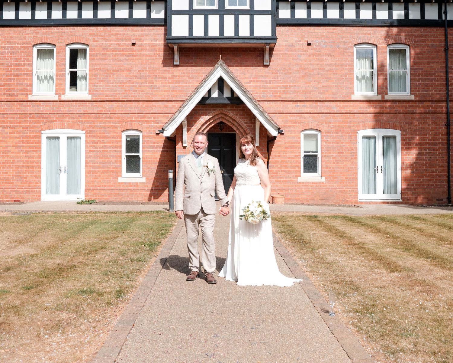 Bride and groom holding hands outside a red brick Tudor-style building on their wedding day.