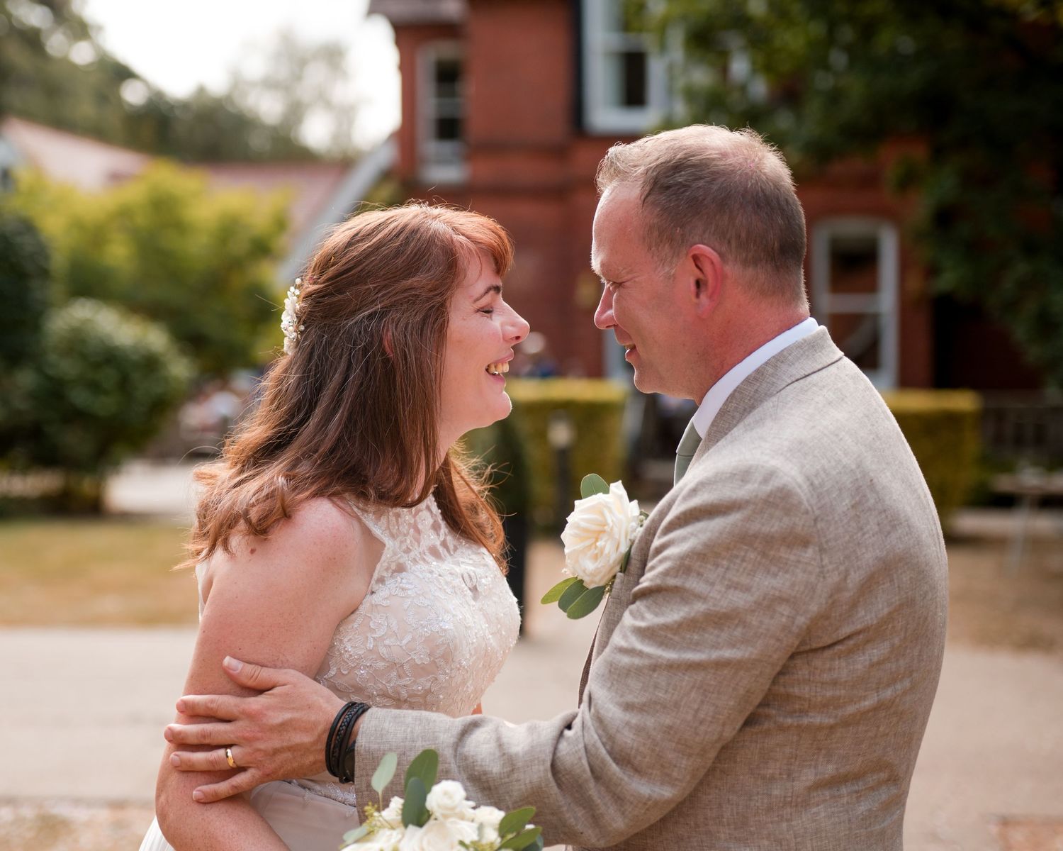 A bride and groom share a tender moment outdoors, smiling at each other on their wedding day.