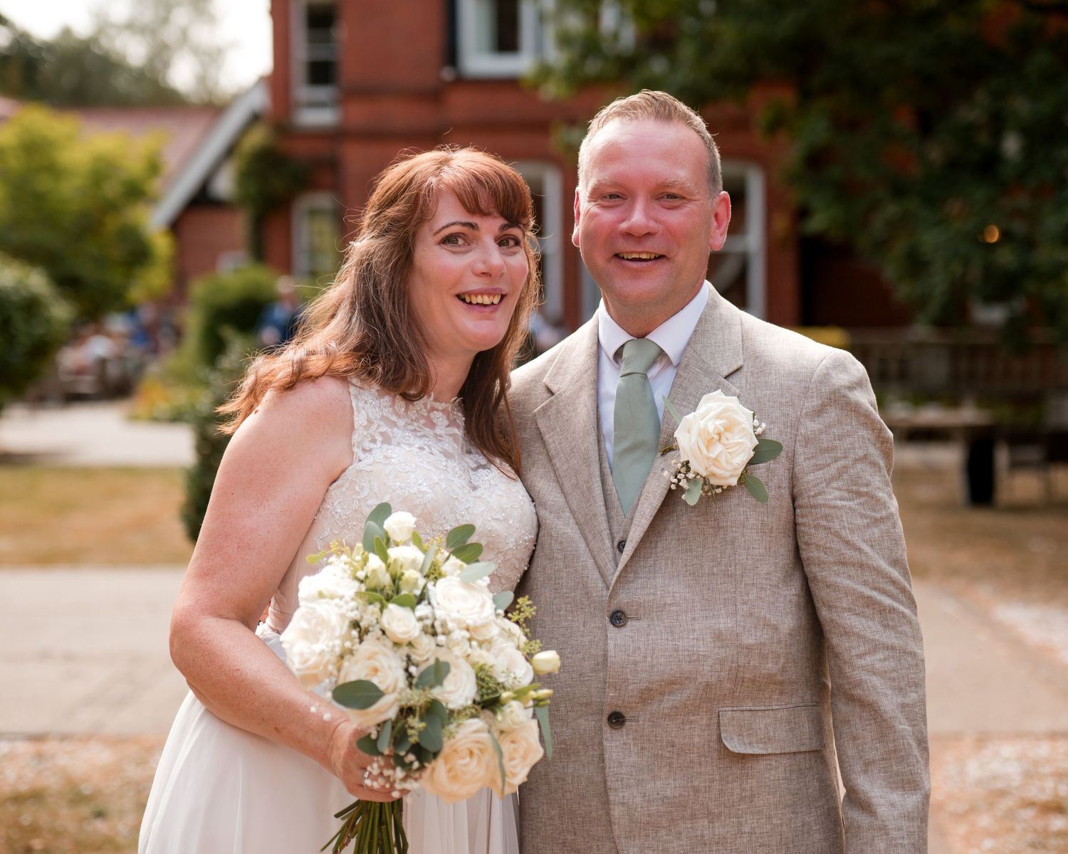 Smiling bride and groom posing together outdoors on their wedding day, bride holding white bouquet.