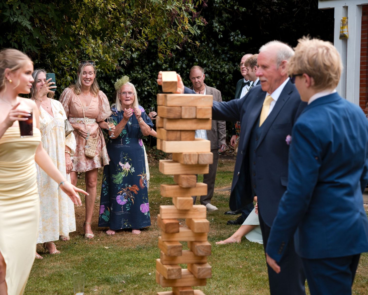 Guests playing giant Jenga outdoors at a summer garden party wedding reception on a sunny day.