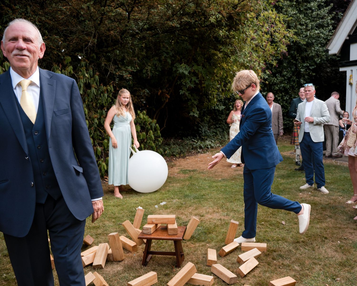 Guests playing giant Jenga at an outdoor wedding reception in a garden setting.