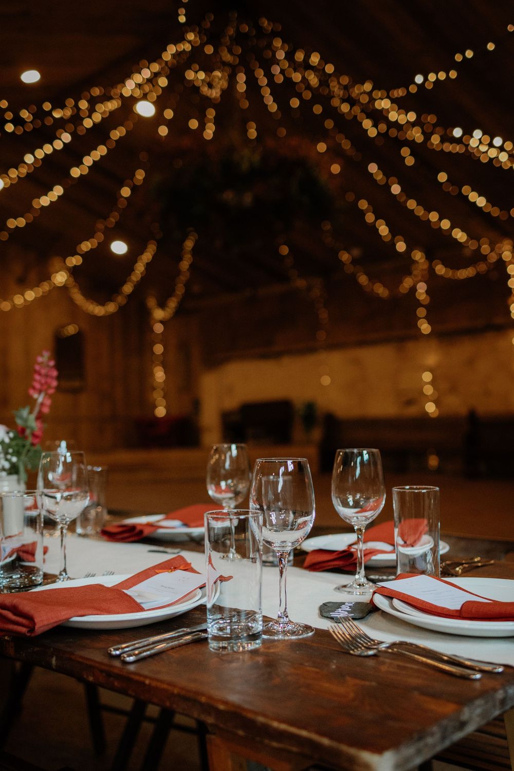 Elegant wedding reception table set with red napkins and crystal glasses, adorned with warm fairy lights draped overhead.