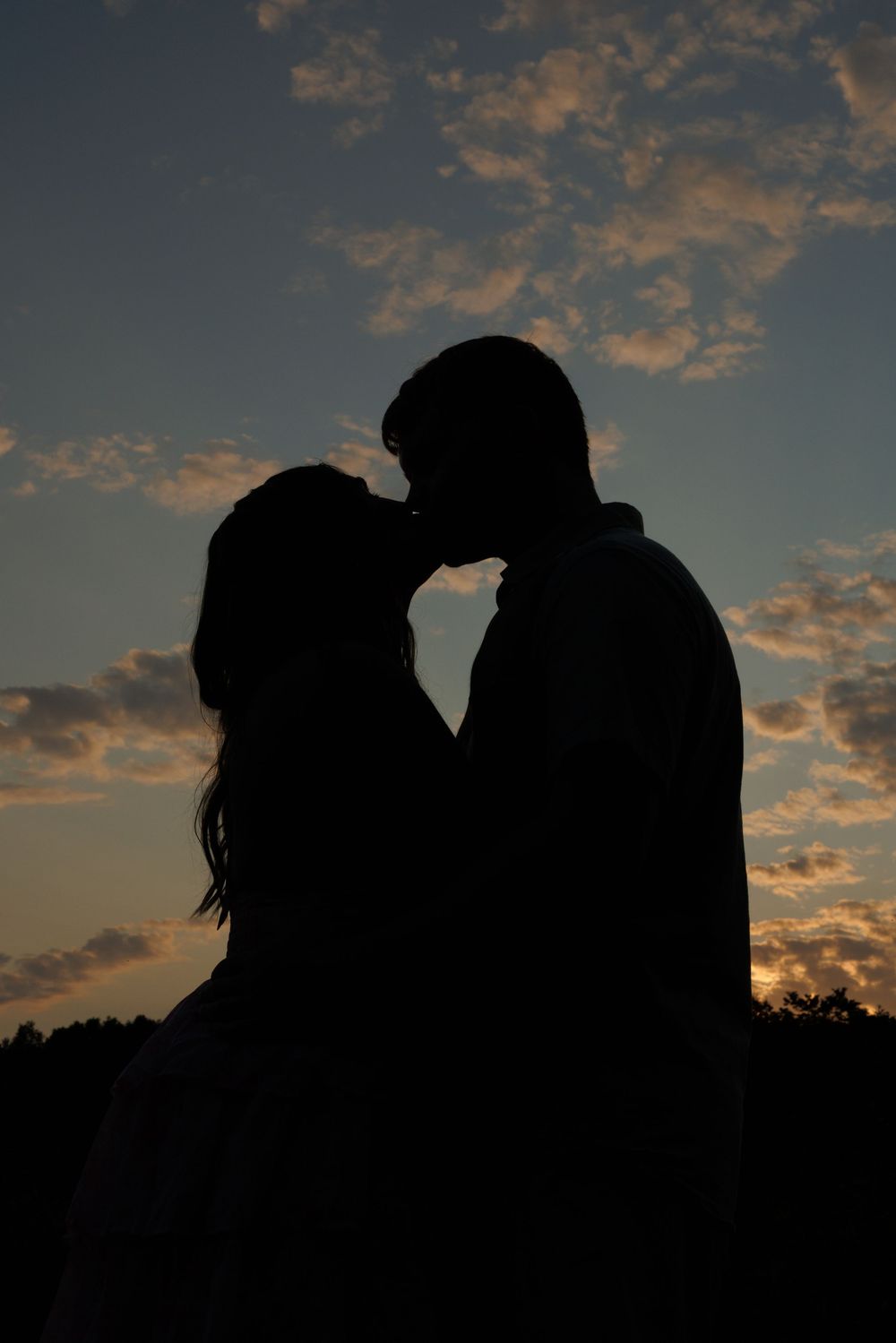 Romantic silhouette of a couple kissing against a stunning sunset sky with golden clouds.