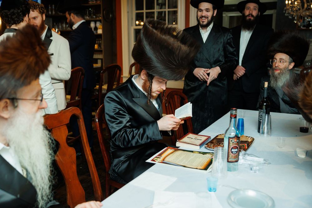 Orthodox Jewish men in traditional attire gather around a table during a religious ceremony or celebration.