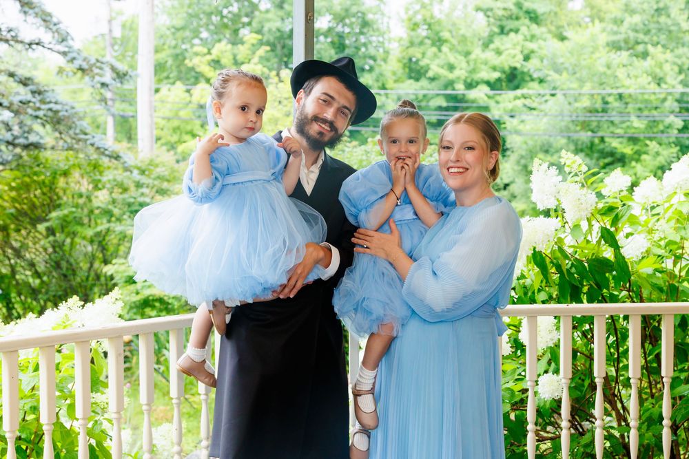 A joyful family in matching blue outfits poses outdoors, with a man in a black hat holding two young girls.