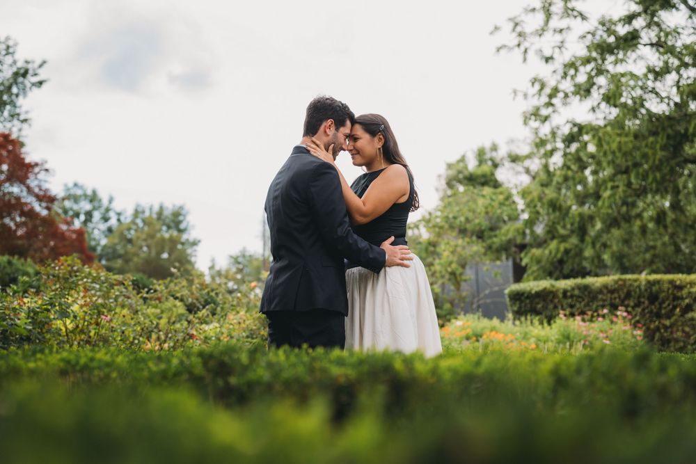 Couple embracing romantically in a lush garden, dressed in elegant attire for an engagement or wedding photo session.