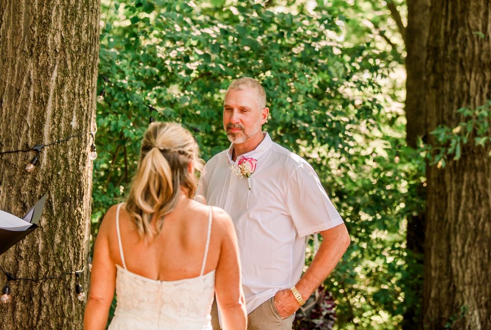 Bride and groom share a romantic first look moment outdoors among tall trees with lush green foliage.