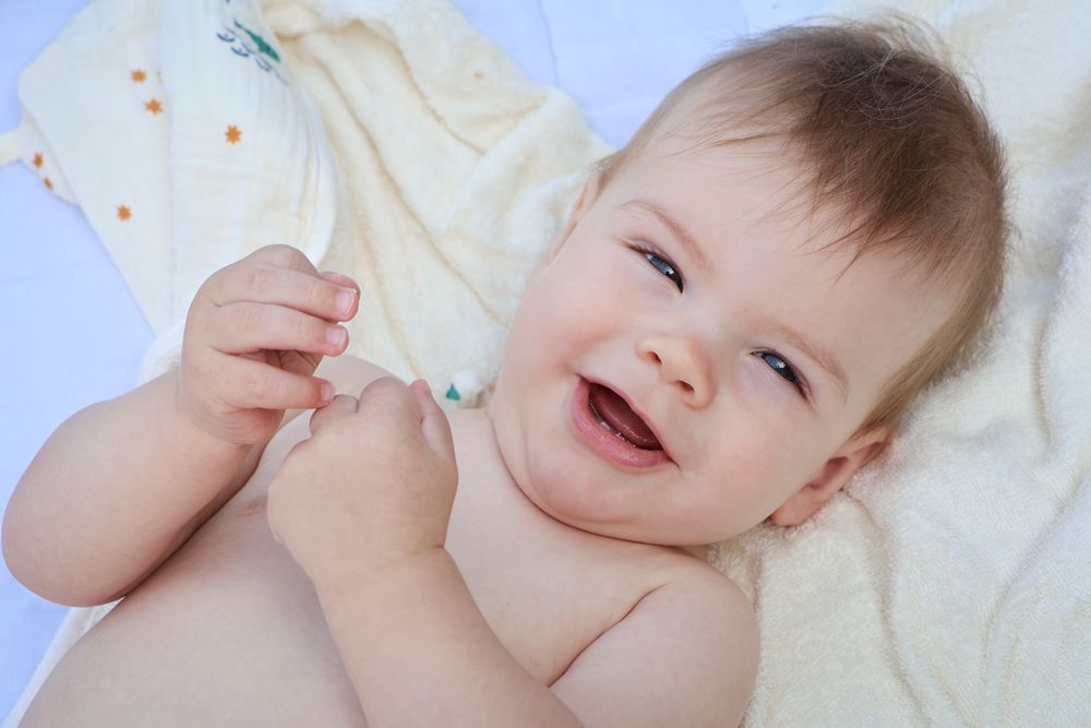 Bébé souriant allongé sur une couverture crème, séance photo bébé et famille en Ardèche
