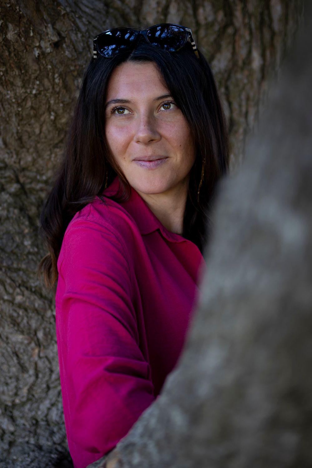 Portrait d’une femme en chemise fuchsia, appuyée derrière un tronc d’arbre, regard de côté, Lyon
