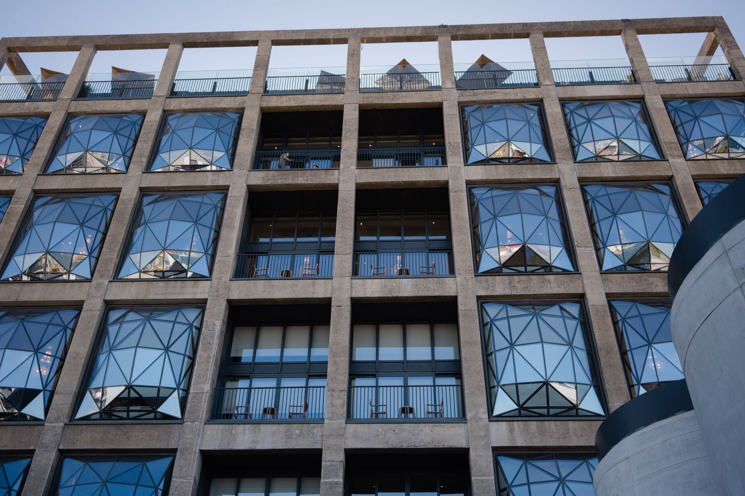 Modern brutalist office building facade with geometric concrete grid and blue glass windows against a clear sky.
