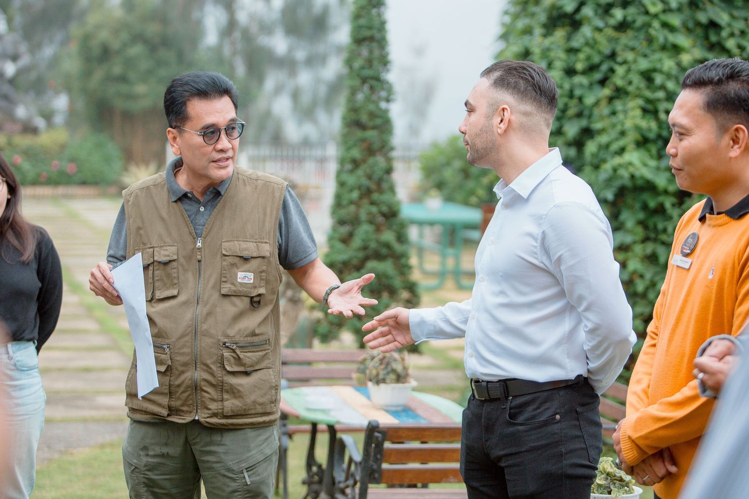 Group of professionals engaged in outdoor discussion, with men in casual and business attire conversing in a garden setting.