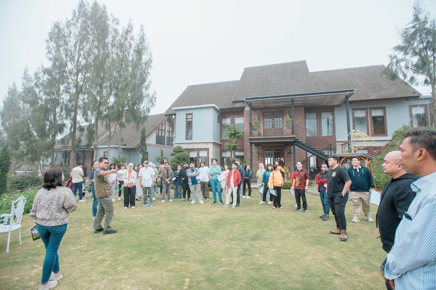 Large group of people gathered on green lawn in front of a colonial-style building on a foggy day.