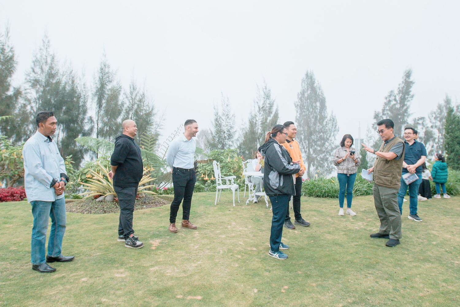 Group of people socializing on a lush green lawn outdoors on a misty day.