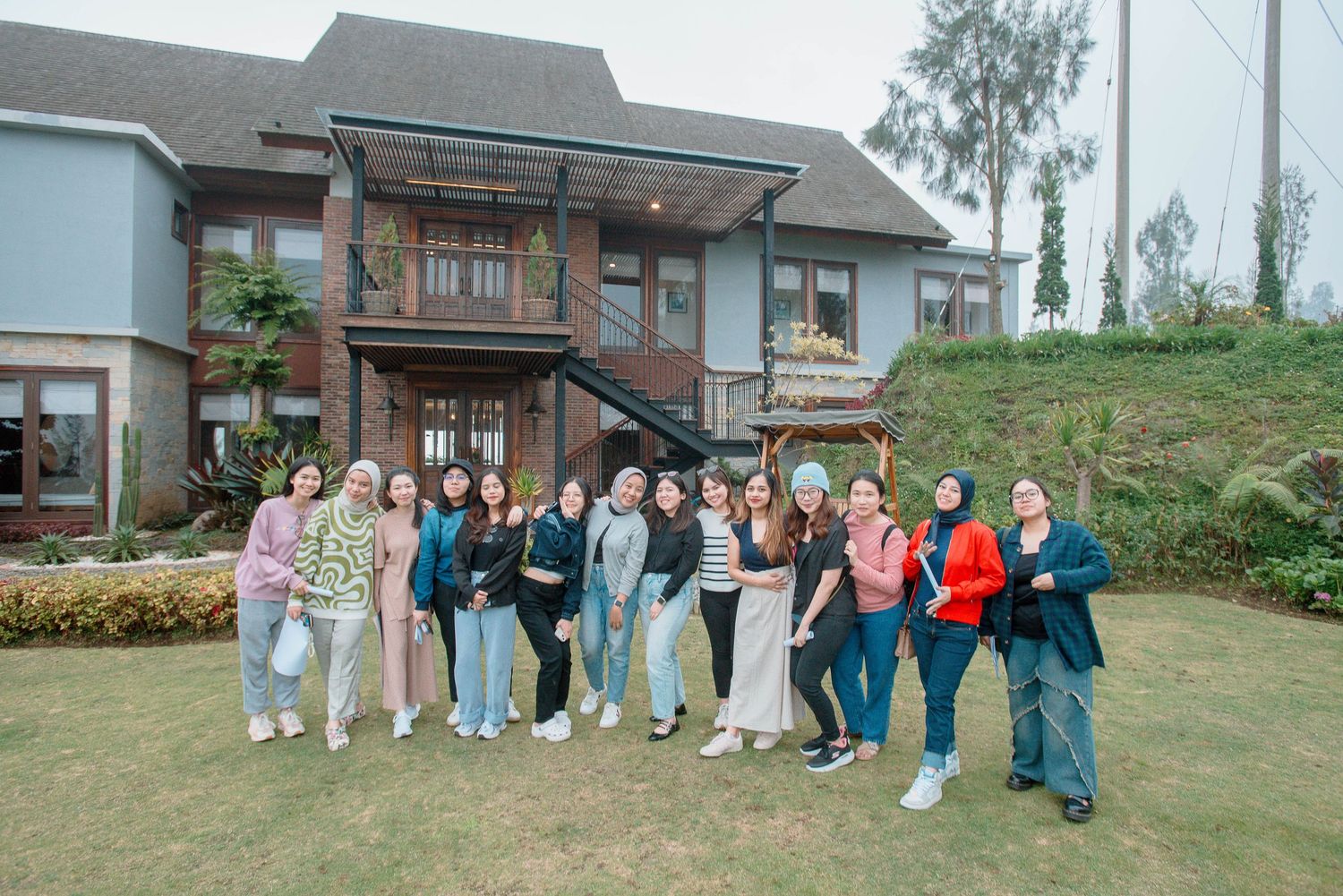 Group of women posing together in front of a modern two-story house on a green lawn.