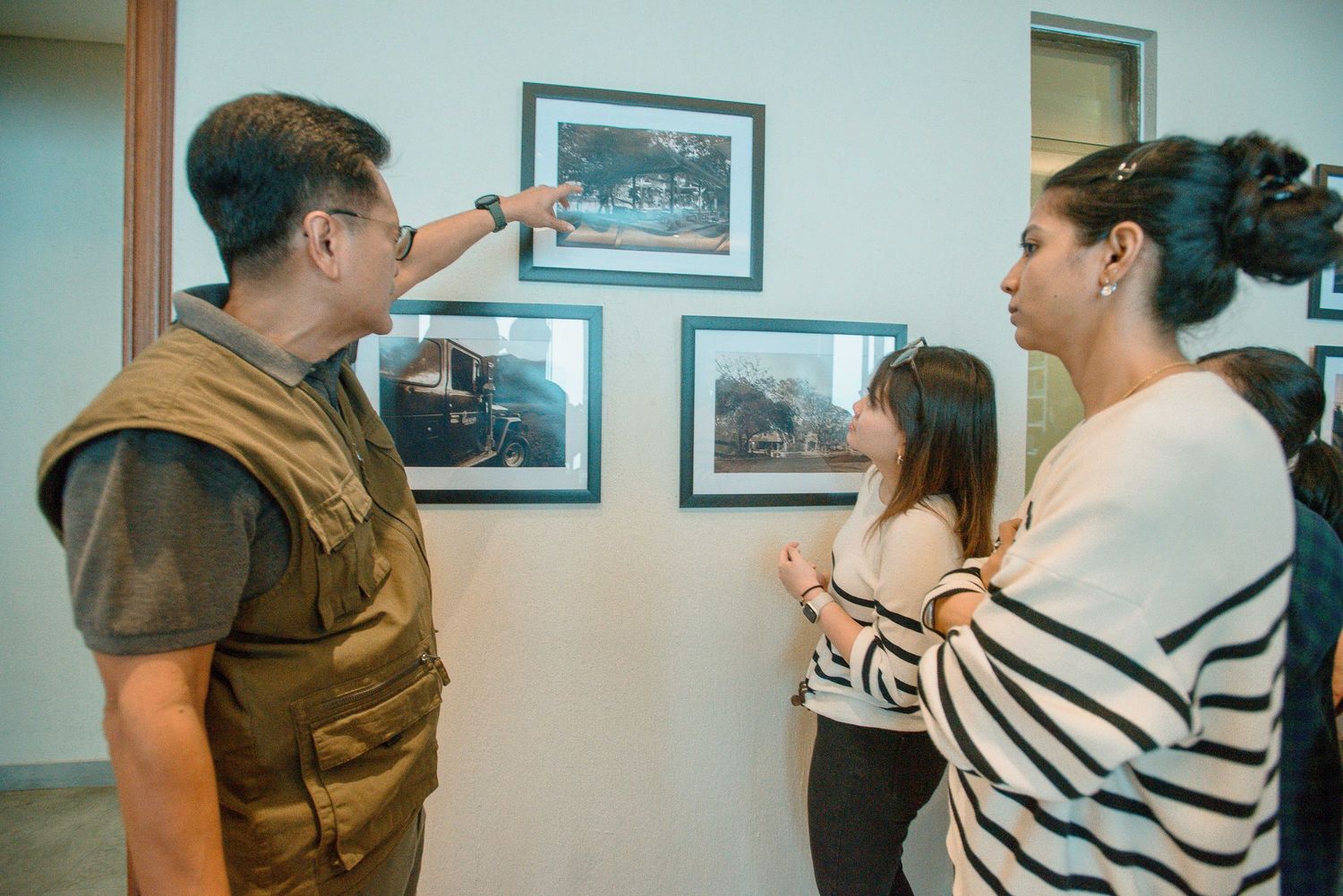 Three people examining framed photographs displayed on a gallery wall during an art exhibition.