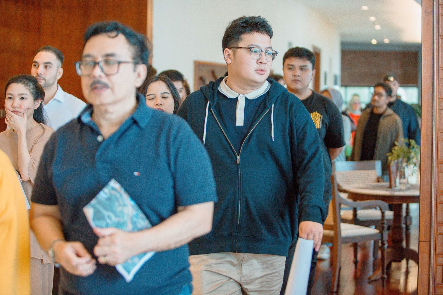 Group of people entering a modern restaurant, led by two men wearing glasses in casual attire.