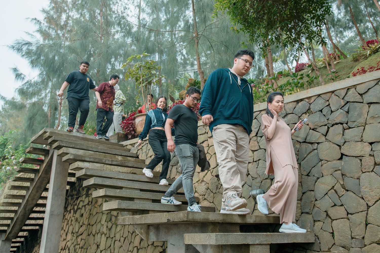 Group of friends walking down outdoor stone steps surrounded by lush trees and a stone retaining wall.