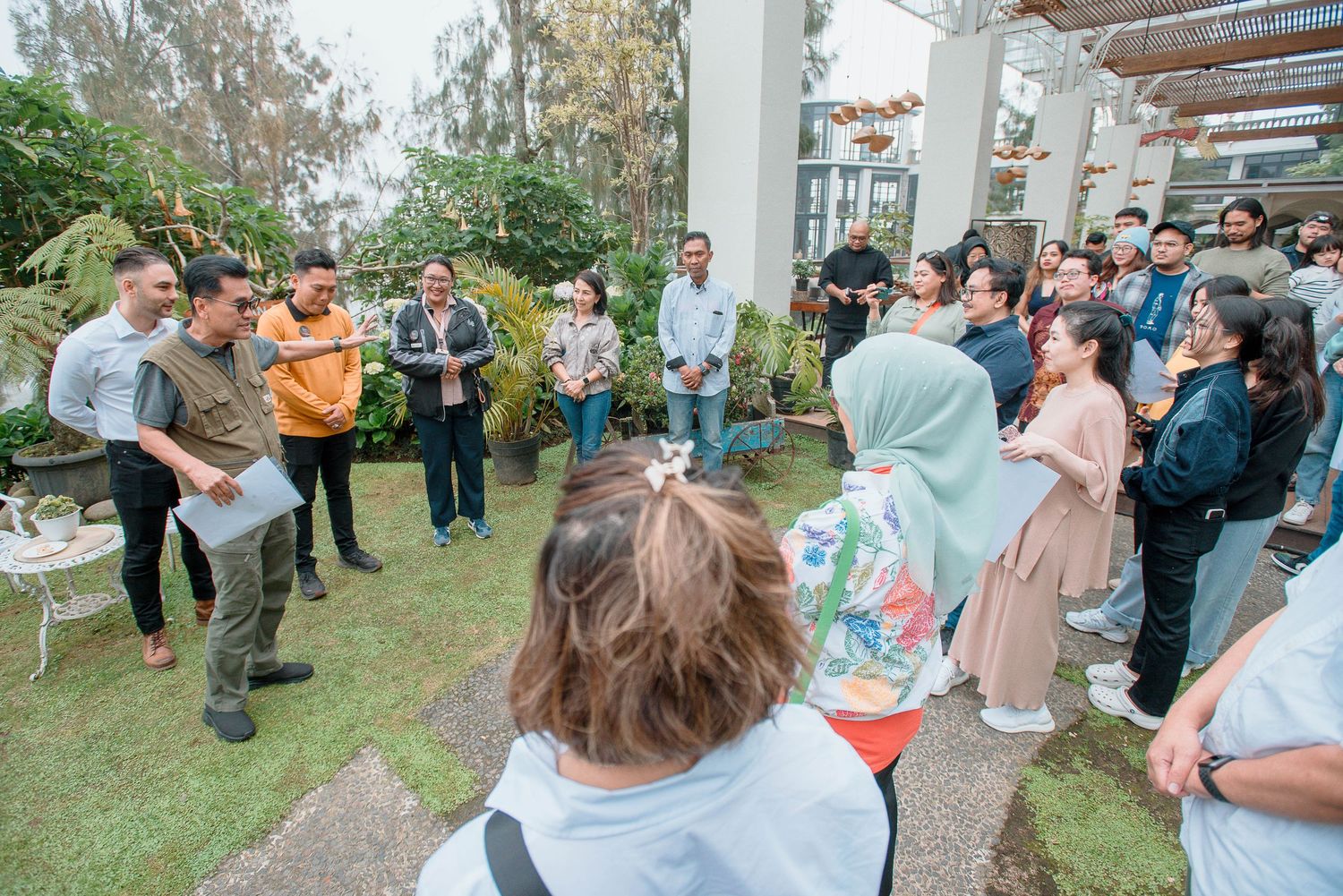 Group of people gathered outdoors on a lawn for a casual meeting or event in a garden setting.