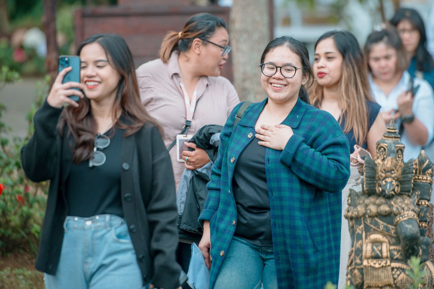 Group of young women smiling and taking photos outdoors near ornate stone sculptures.
