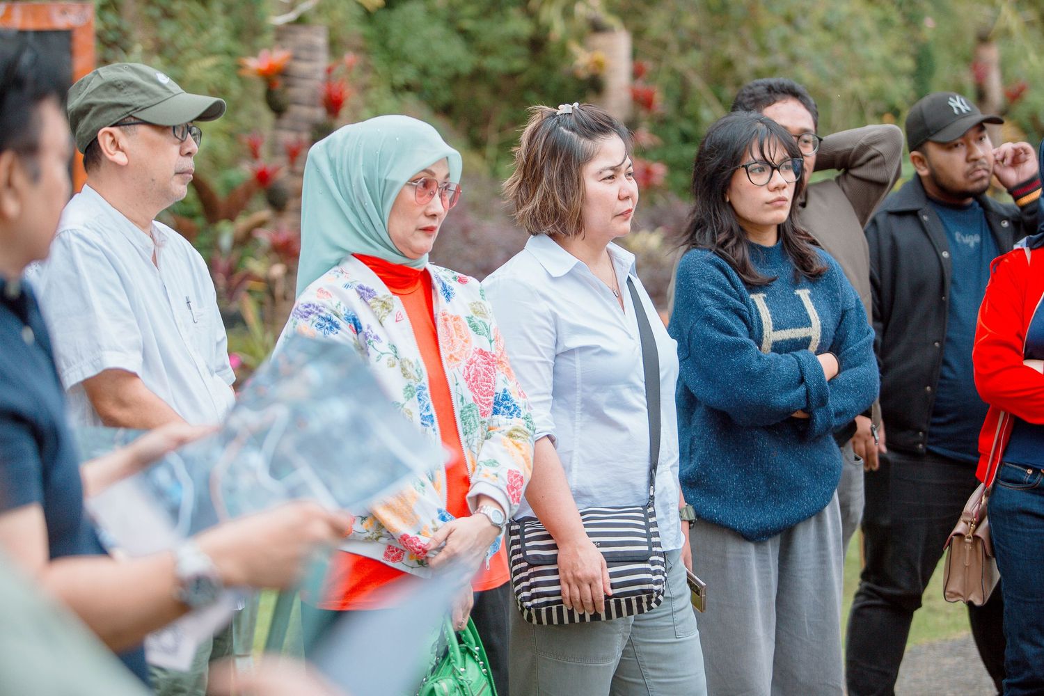 A diverse group of people standing outdoors at a cultural event, including a woman in a hijab and floral jacket.