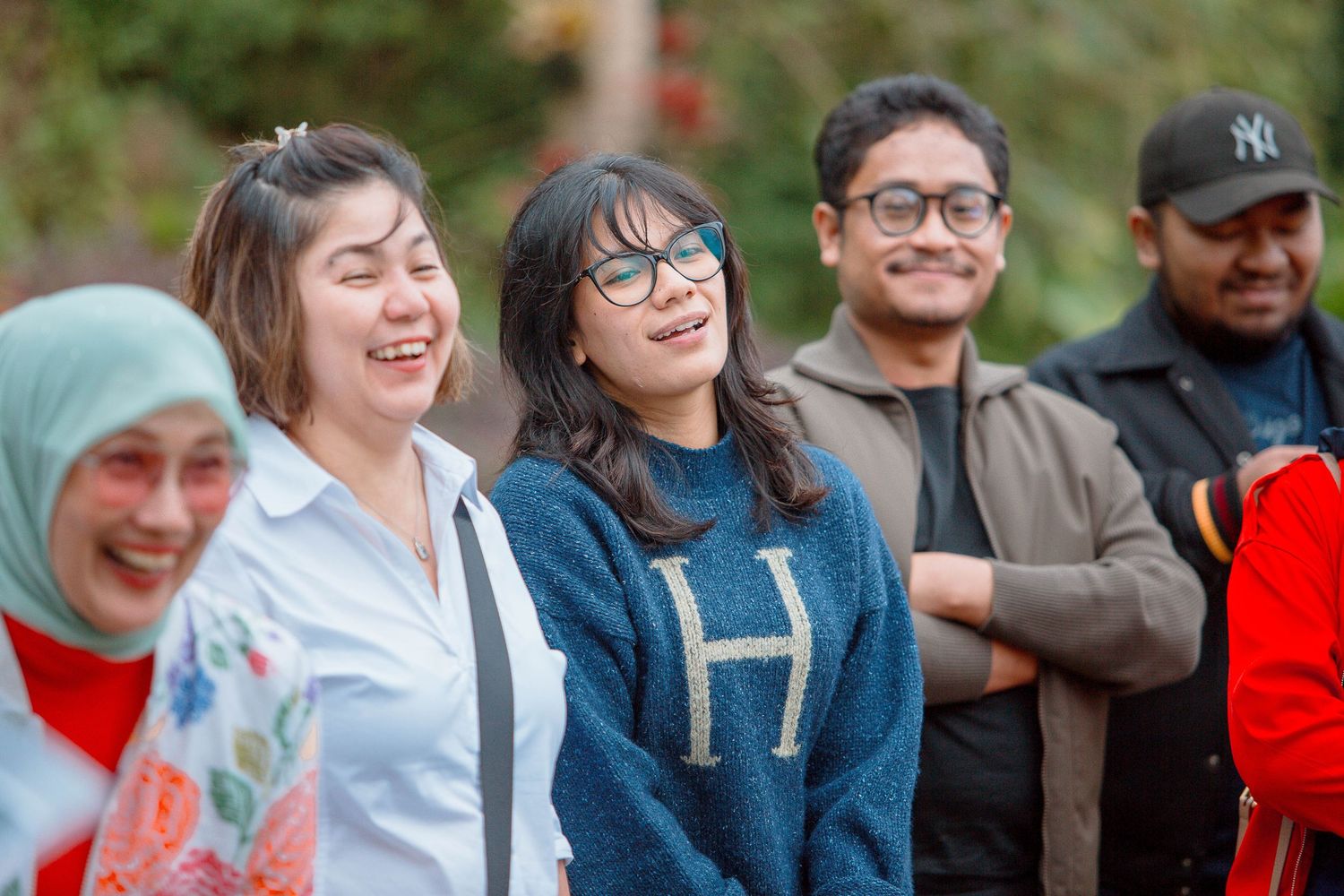 A diverse group of young adults laughing and smiling outdoors, enjoying a fun social gathering together.
