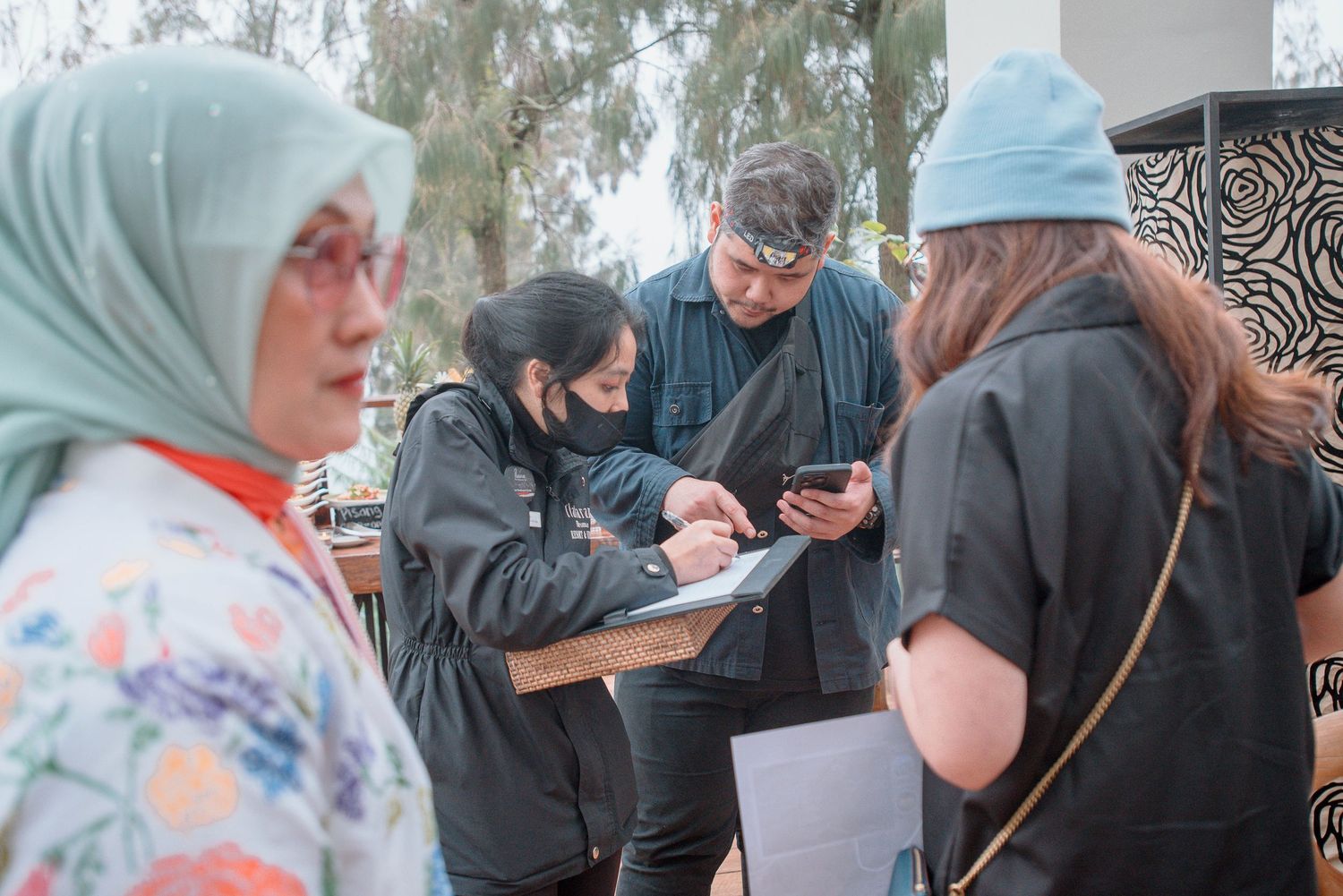 Group of people in black uniforms reviewing documents and phone outdoors near decorative wall.