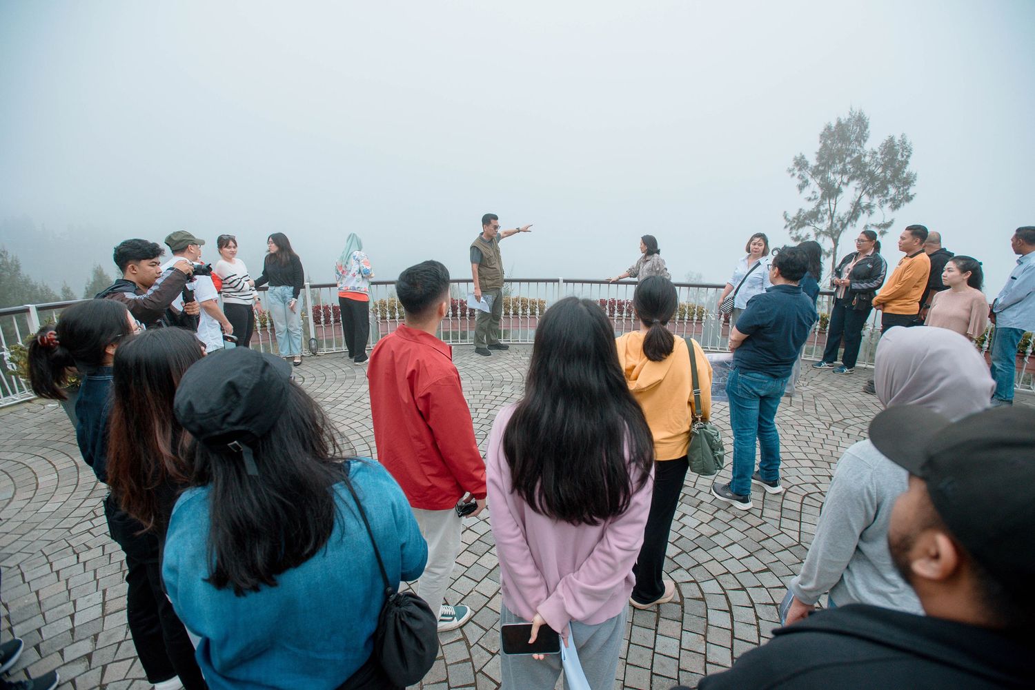 Tourists gather on a foggy mountain viewpoint overlook, standing on a stone terrace surrounded by misty clouds.