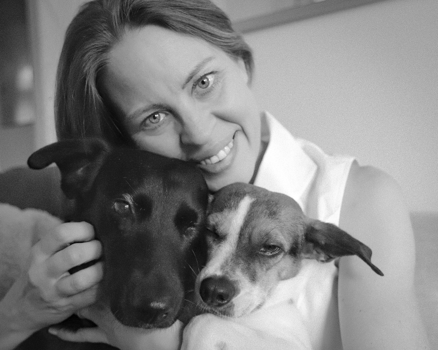 Sarah smiling with her two rescue dogs in a black-and-white portrait.