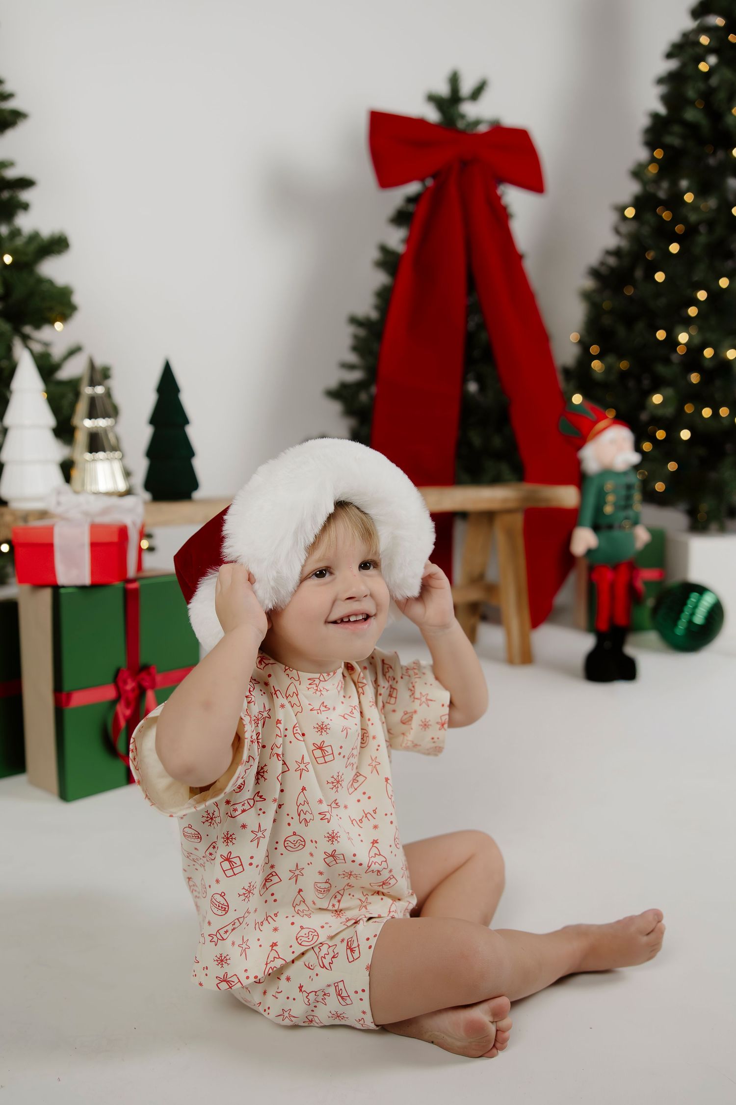 Smiling child wears a Santa hat among festive Christmas decorations during a studio Christmas mini session in Mandurah.