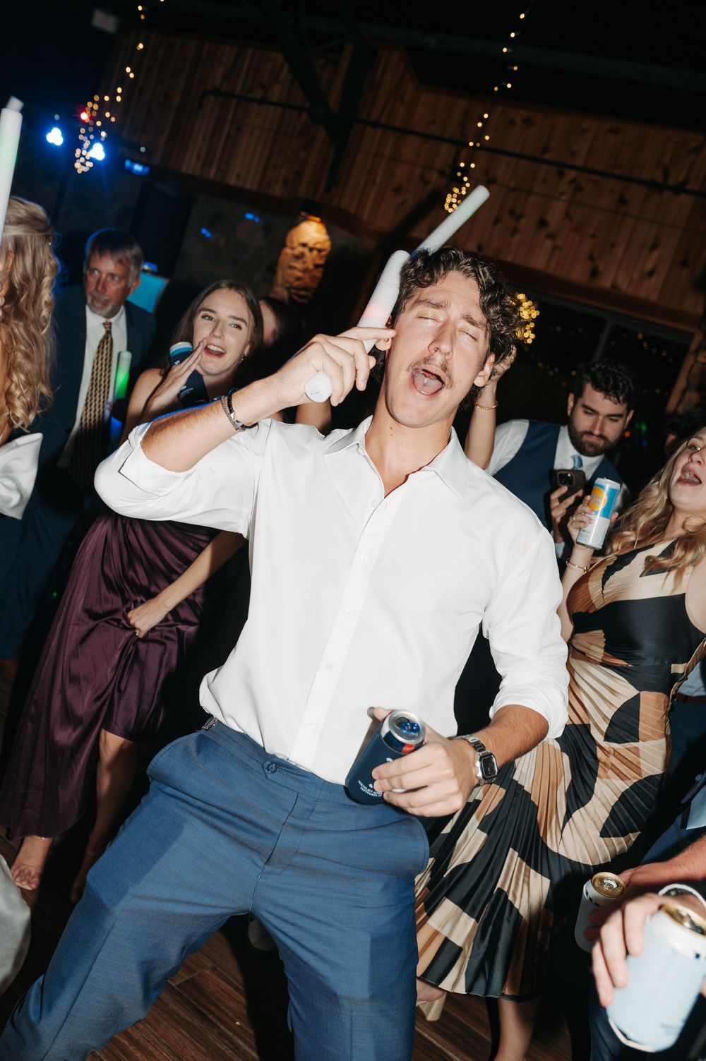 Man in white shirt dancing energetically at a wedding reception party with guests celebrating in background.